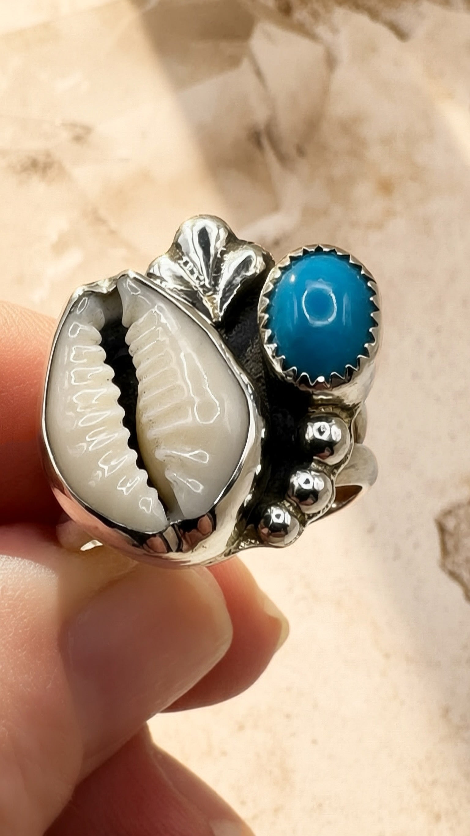 Silver ring with a cowrie shell and Bisbee turquoise stone held against a beige background
