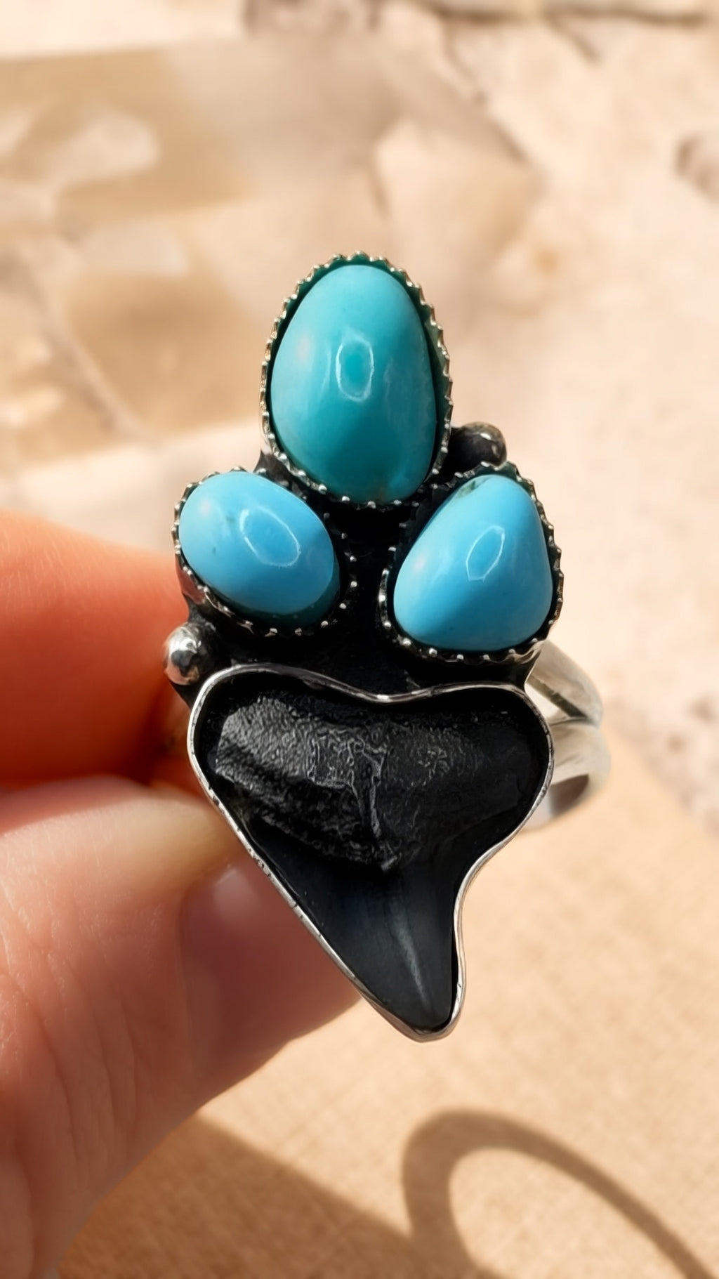 Ring with turquoise stones and black shark tooth held by a hand against a neutral background