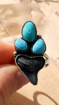 Ring with turquoise stones and black shark tooth held by a hand against a neutral background