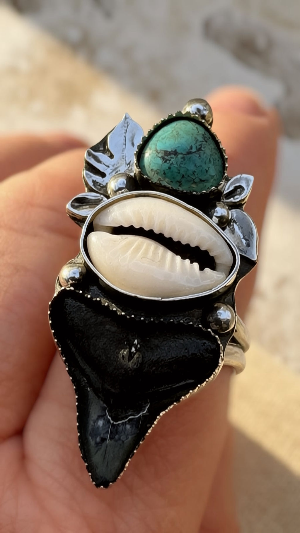 Ring with black shark tooth, white shell, and green turquoise on a hand