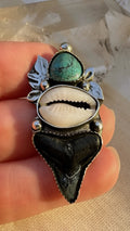 Hand holding a decorative ring with shell, turquoise stone, and black shark tooth.
