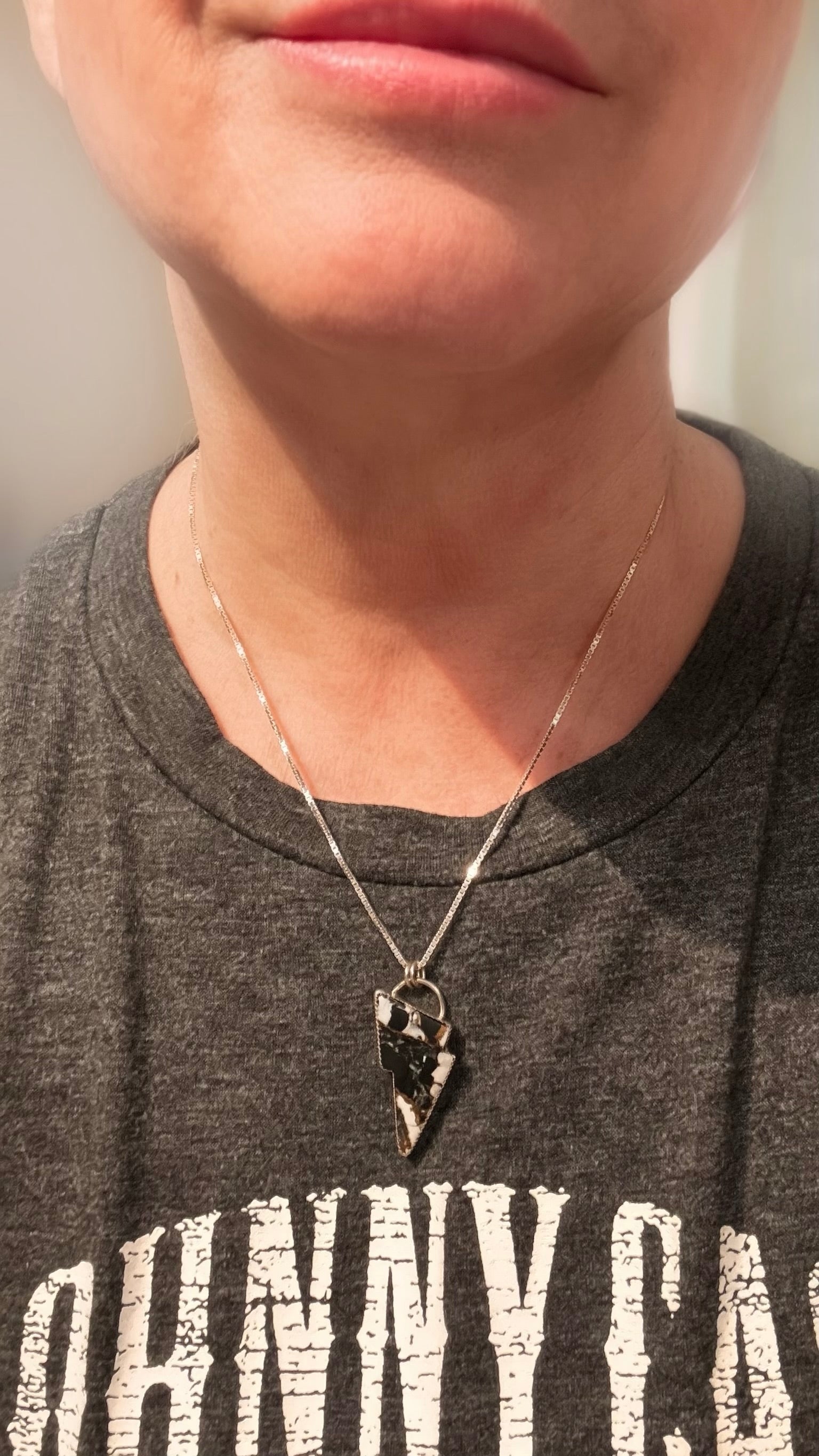 Person wearing a necklace with an lightning bolt  pendant, against a neutral background