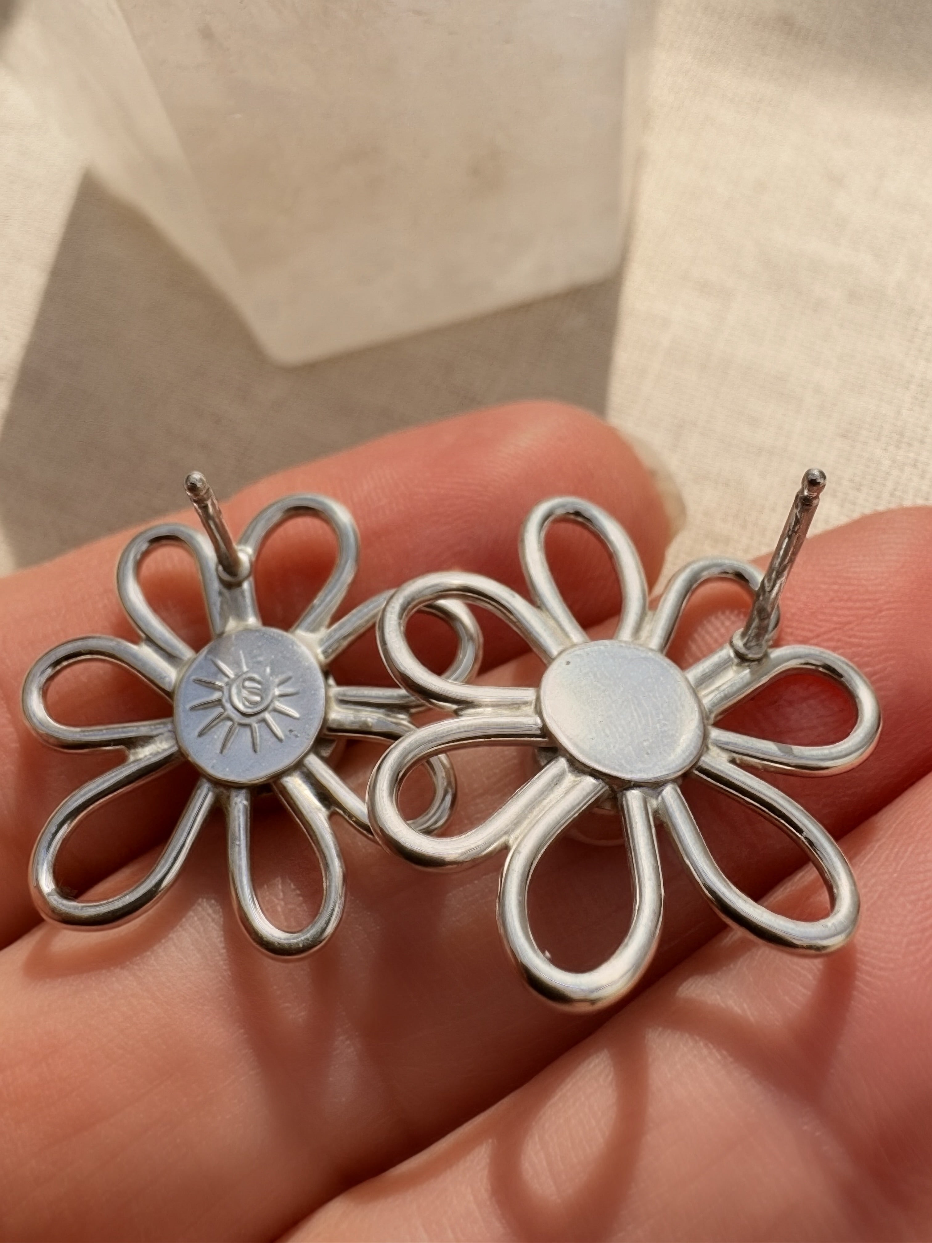Silver flower-shaped earrings held in a hand with a neutral background