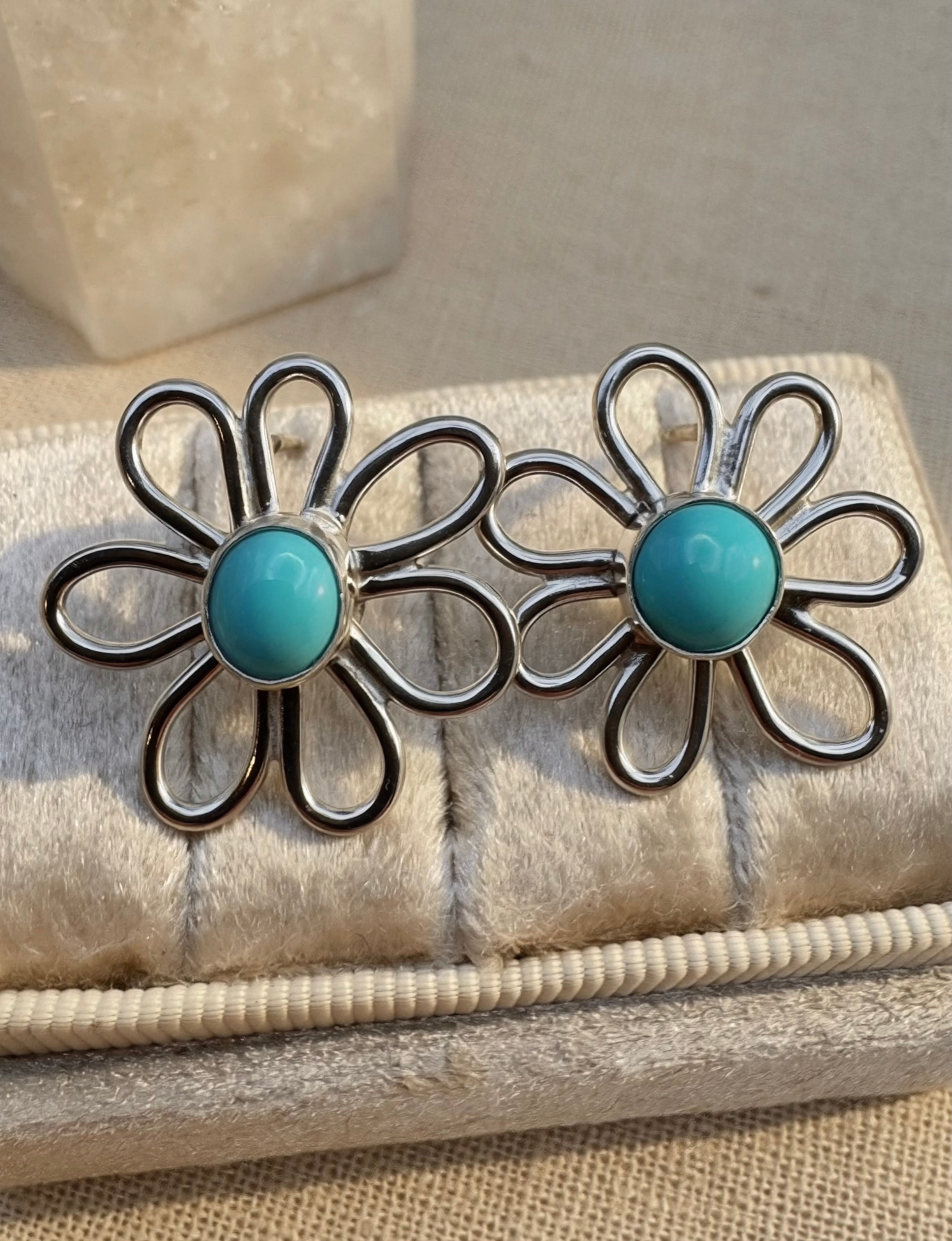 Pair of silver flower-shaped earrings with turquoise centers on a textured surface.
