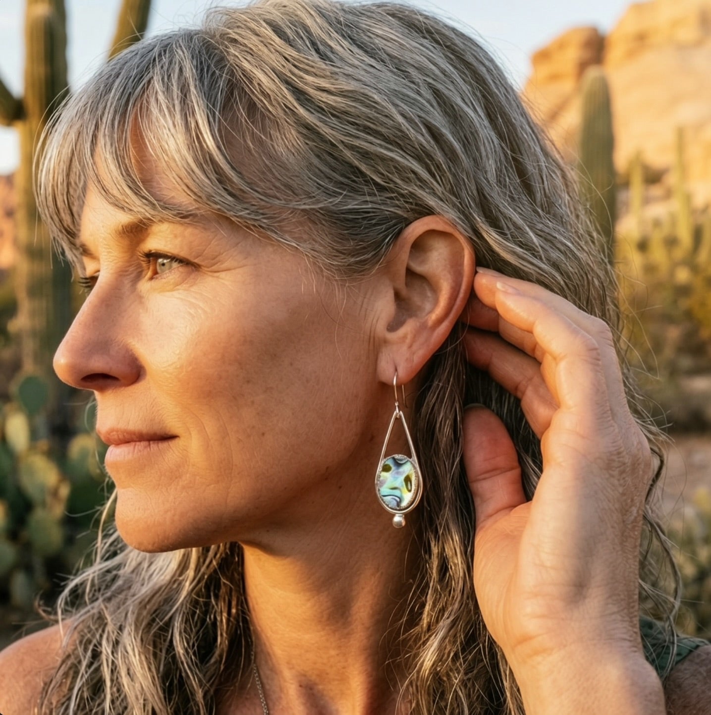 Woman wearing abalone shell drop earrings in desert sunset light, showing movement and iridescence of natural shell