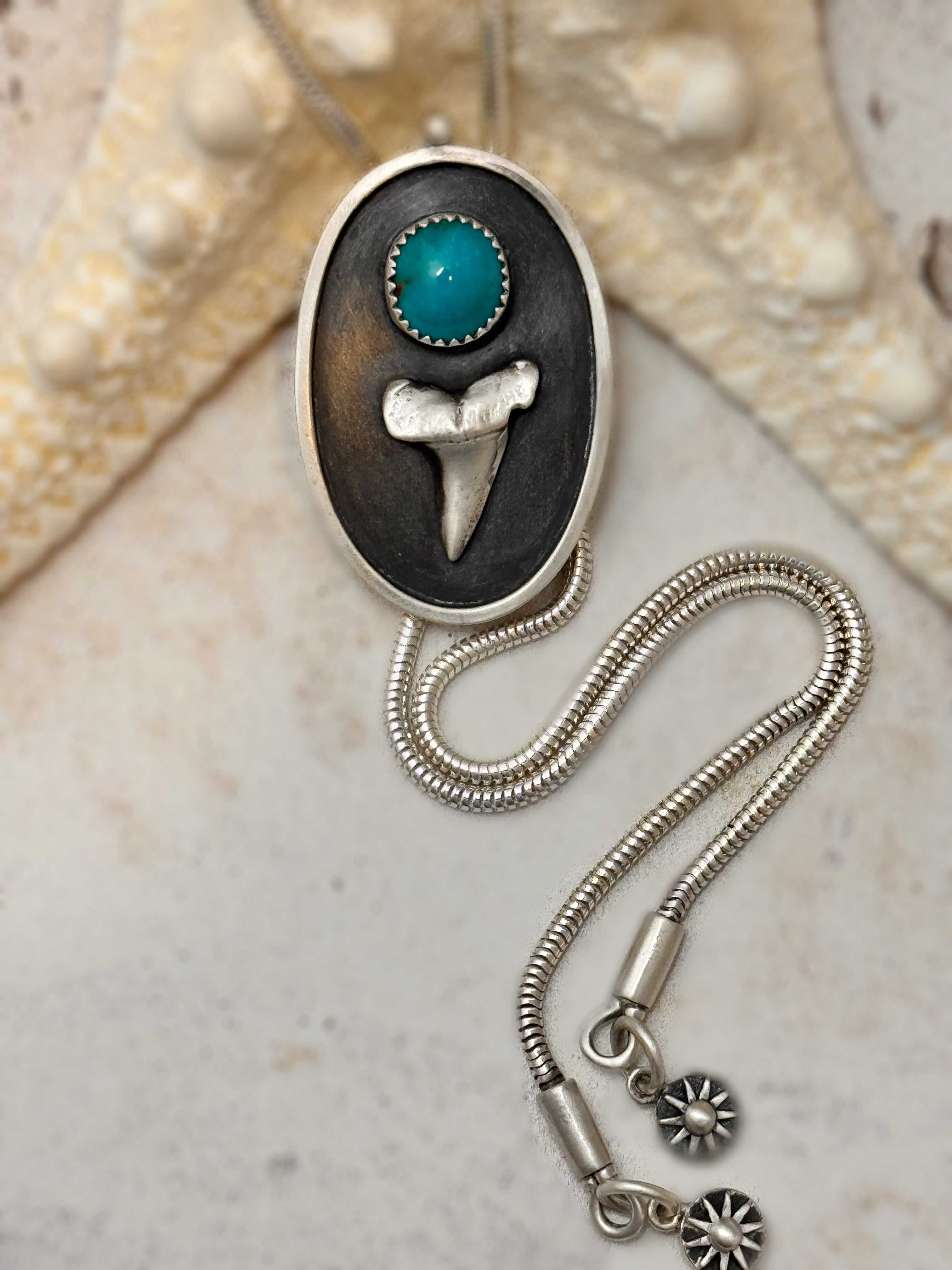 Silver necklace with pendant featuring Bisbee turquoise stone and shark tooth on seashell background