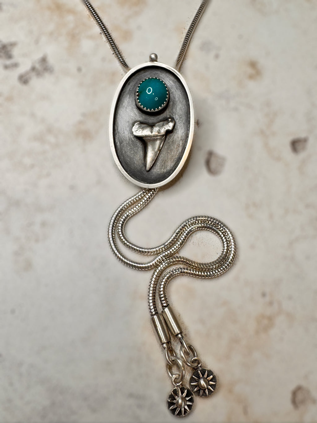 Silver necklace with pendant featuring a shark tooth and Bisbee turquoise design on a textured beige background