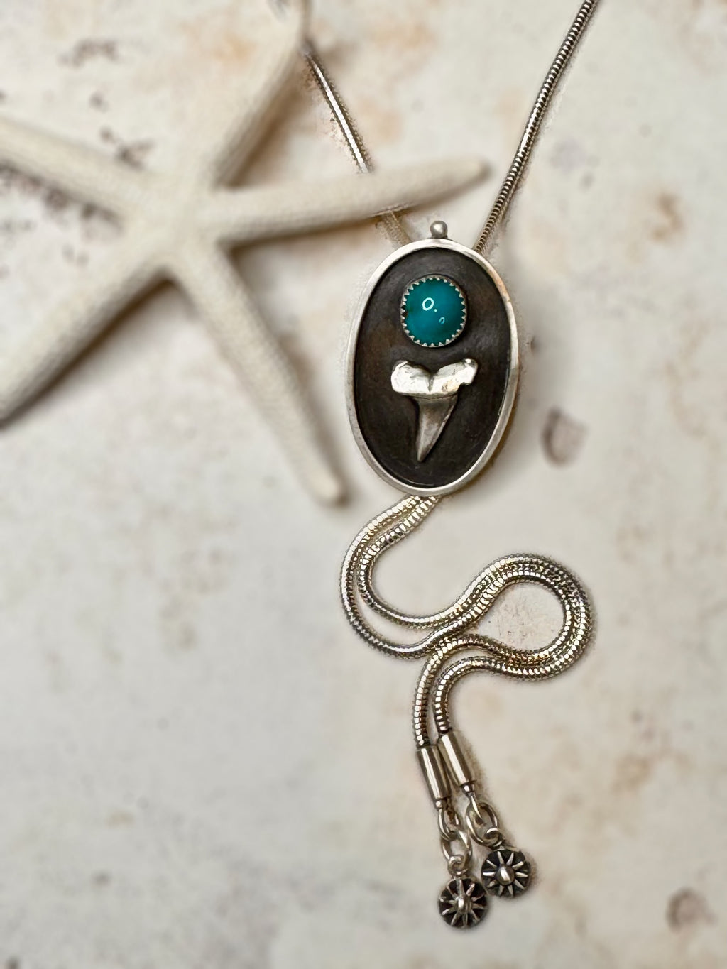 Bolo Necklace with pendant featuring a Bisbee turquoise stone and silver chain on a textured surface.