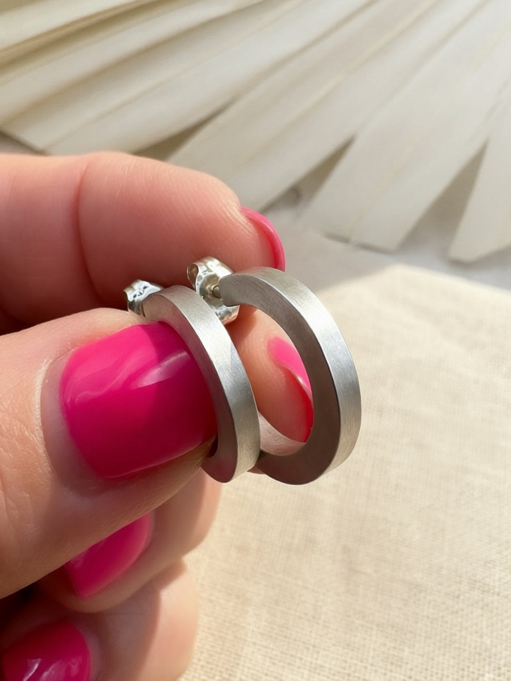 Pair of sterling silver hoops held between fingers, showing flat outer surfaces and a satin finish.