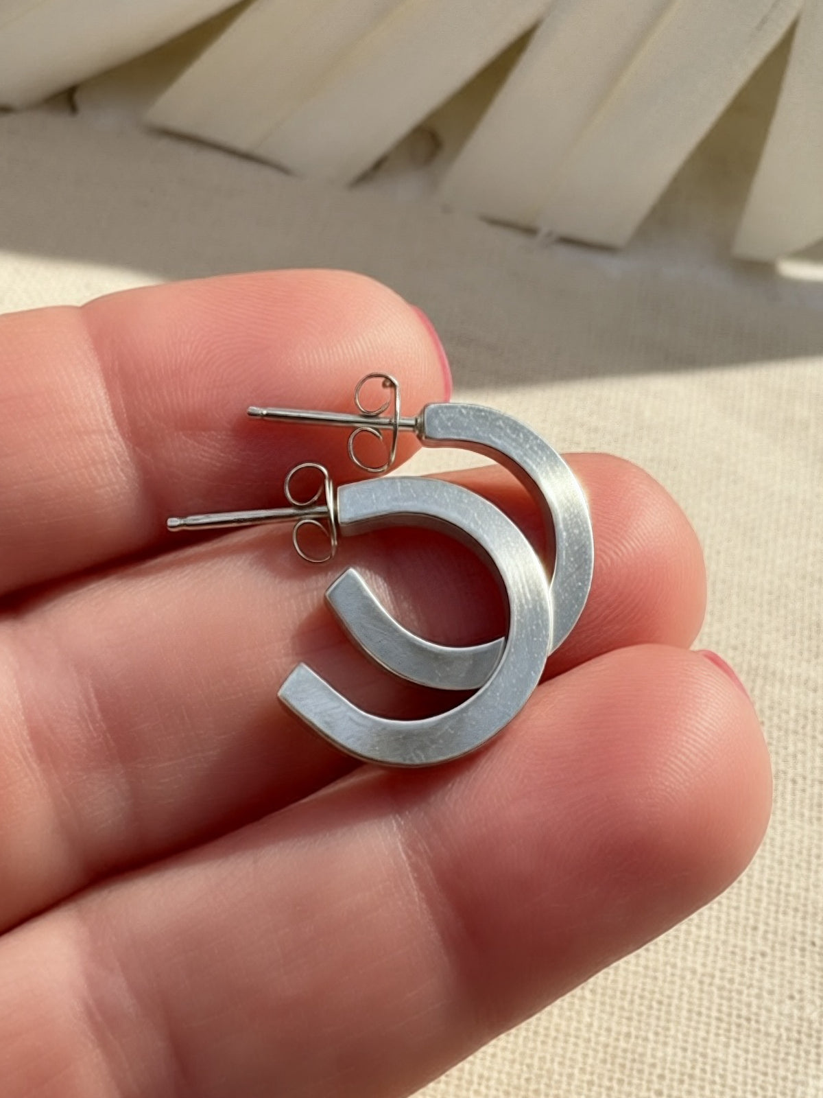 Sterling silver hoops resting across fingers, showing open circular shapes, flat faces, and post closures.