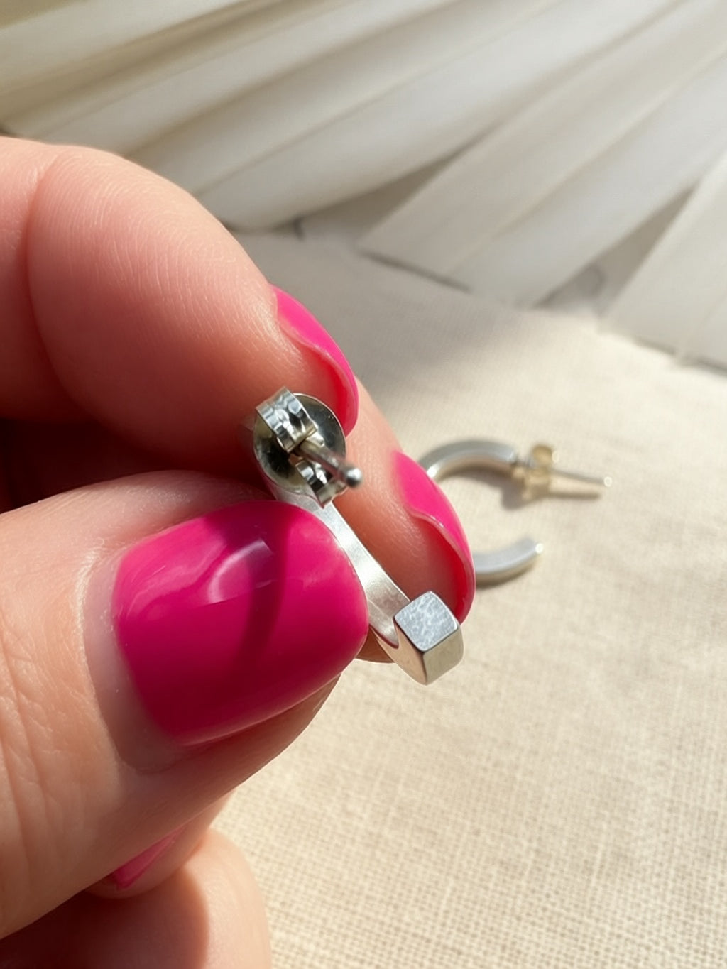 Close view of a silver hoop’s square end and post with butterfly back, held between fingers.