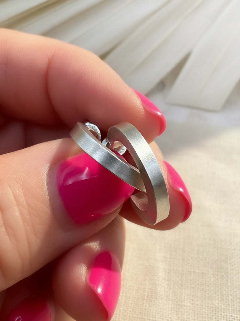 Angled view of satin sterling silver hoops held between fingers, showing their squared profile and thickness.