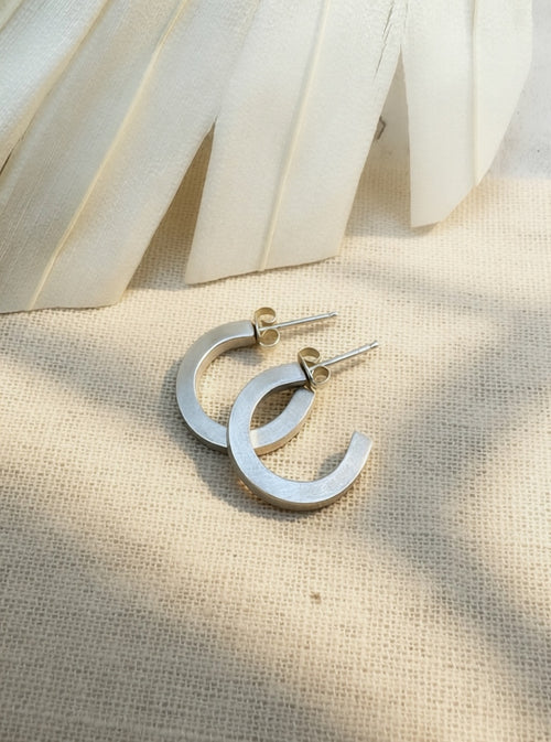 Satin sterling silver hoop earrings on cream fabric, showing flat faces, squared edges, posts, and butterfly backs.