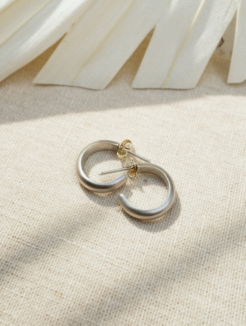Satin sterling silver hoop earrings on cream fabric, showing their open shape, posts, and butterfly backs.