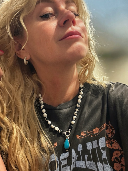 Satin silver hoop worn with a dark graphic T-shirt and a separate beaded turquoise pendant necklace, showing the hoop’s scale.