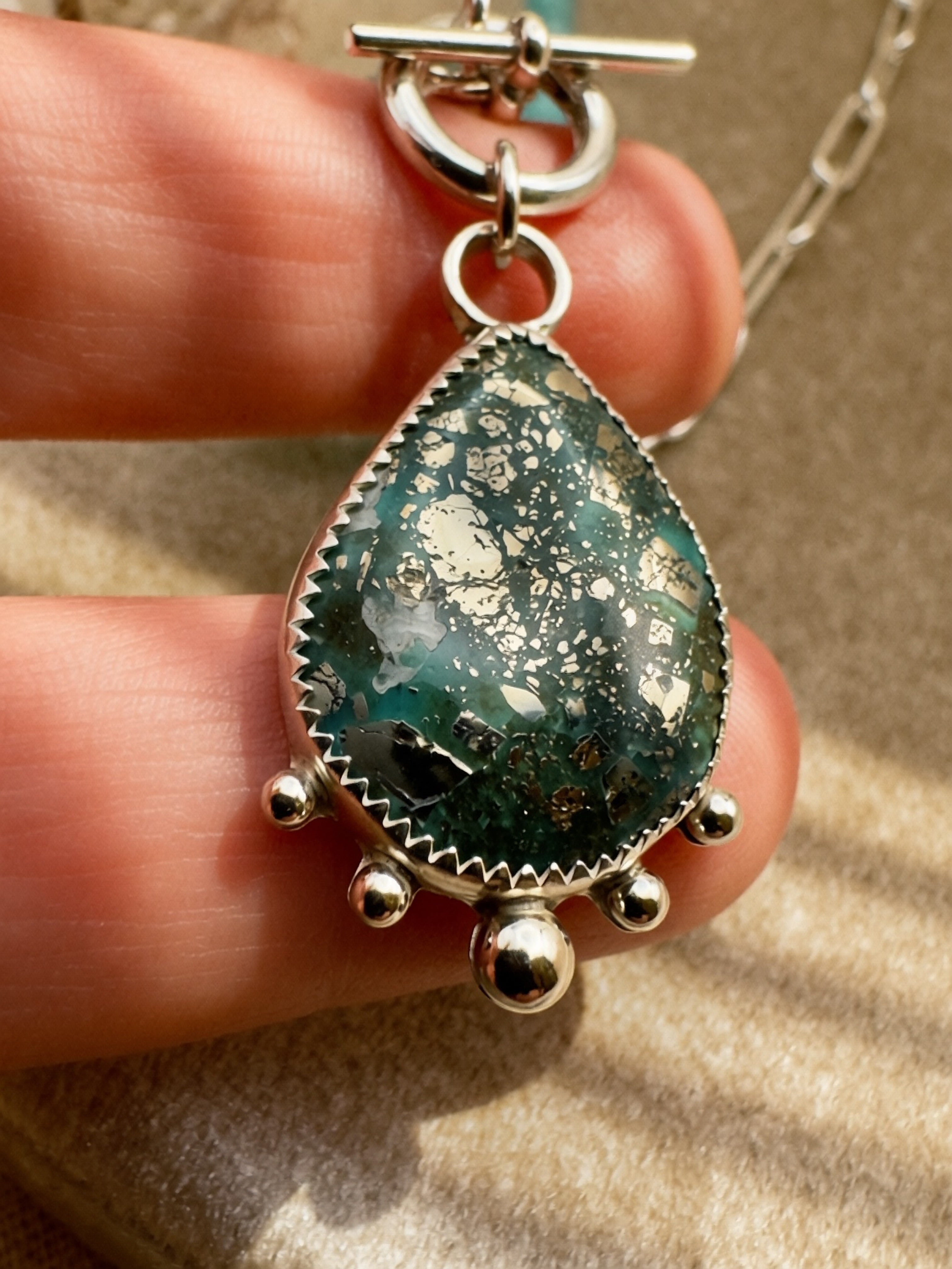 Deep teal turquoise cabochon with pyrite inclusions in serrated bezel setting with sterling silver granulation balls, hand-knotted seafoam bead necklace, Sun Salt Silver