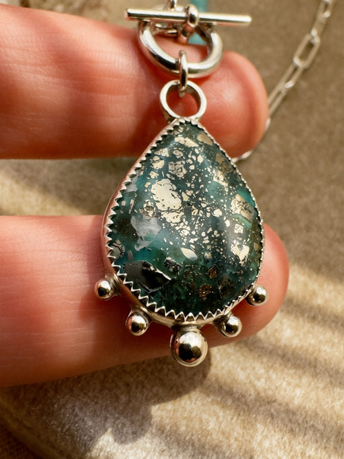 Deep teal turquoise cabochon with pyrite inclusions in serrated bezel setting with sterling silver granulation balls, hand-knotted seafoam bead necklace, Sun Salt Silver