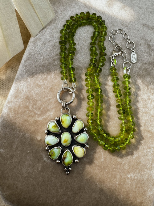 Verdant Sun statement necklace with nine green Palomino variscite stones, hand-knotted peridot beads and a sterling silver charm keeper on a beige background.