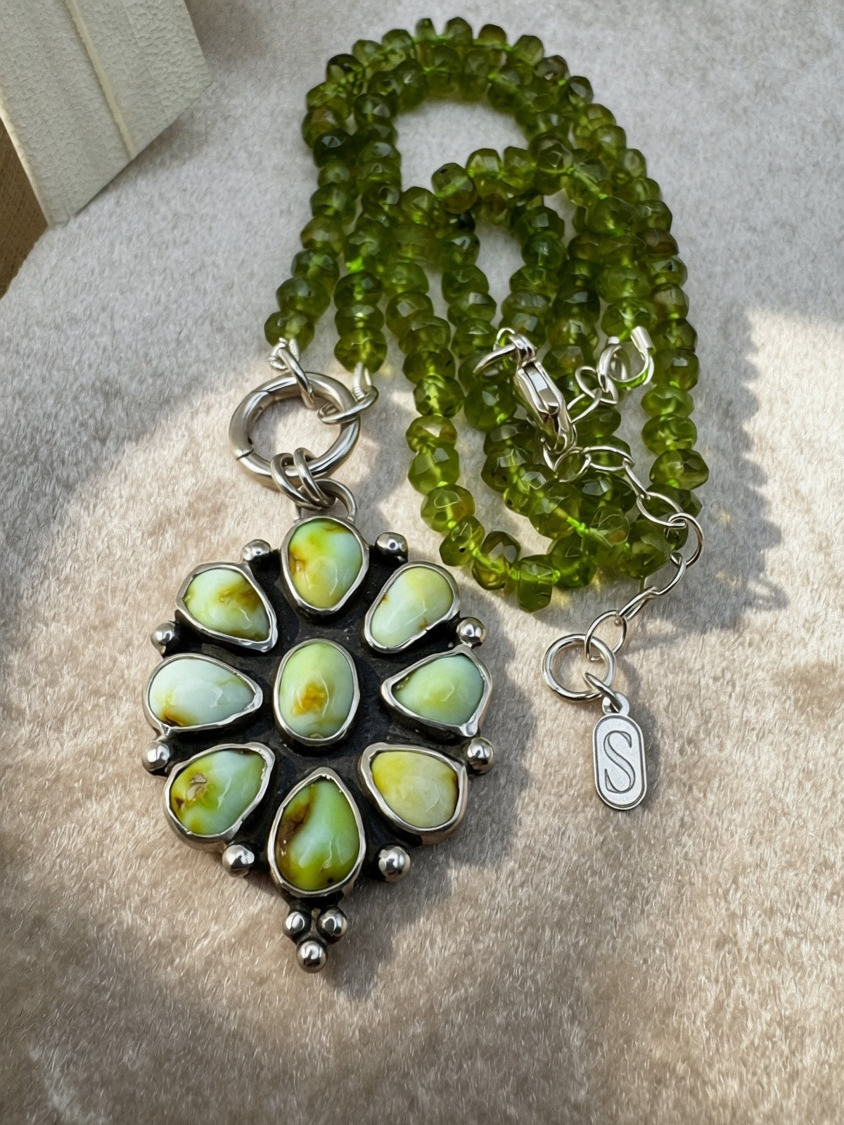 Verdant Sun statement necklace with nine green Palomino variscite stones, hand-knotted peridot beads and a sterling silver charm keeper, on a light background.