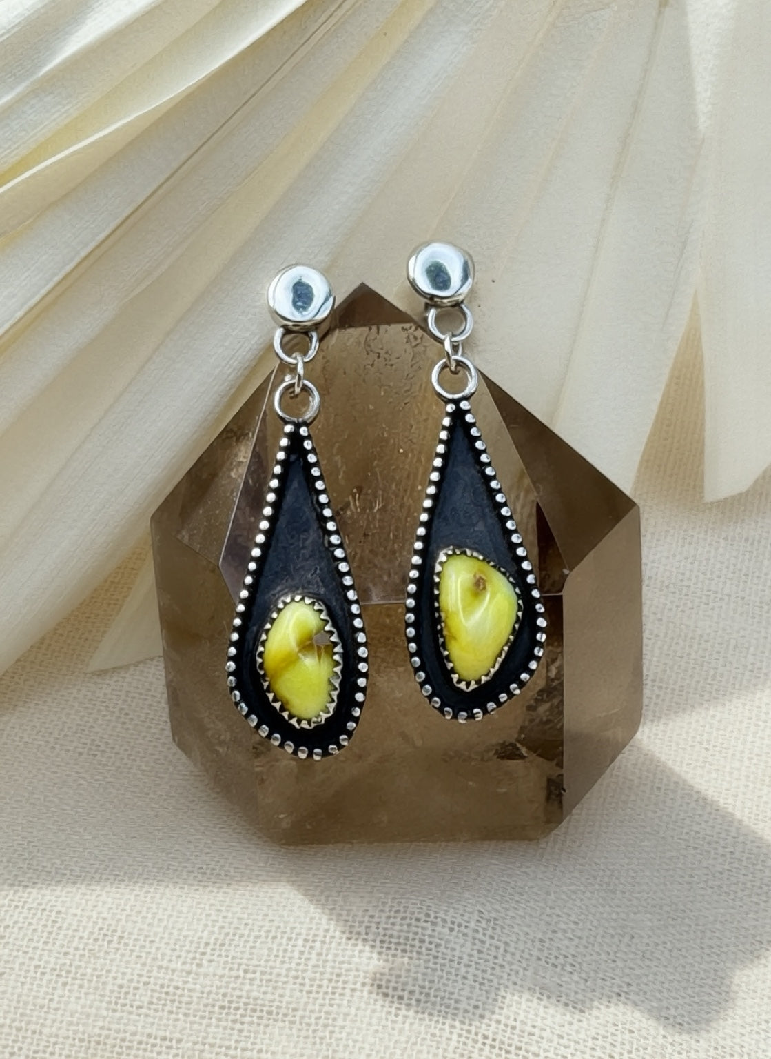 Palomino variscite earrings displayed against a brown crystal, showing elongated teardrop frames and bright silver bead borders.