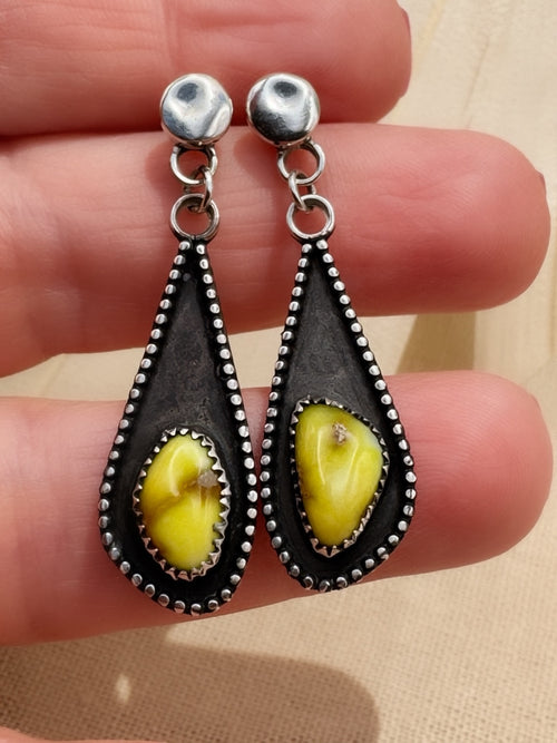 Close view of the earrings across fingers, showing the stones’ differing shapes, serrated bezels, and darkened silver recesses.