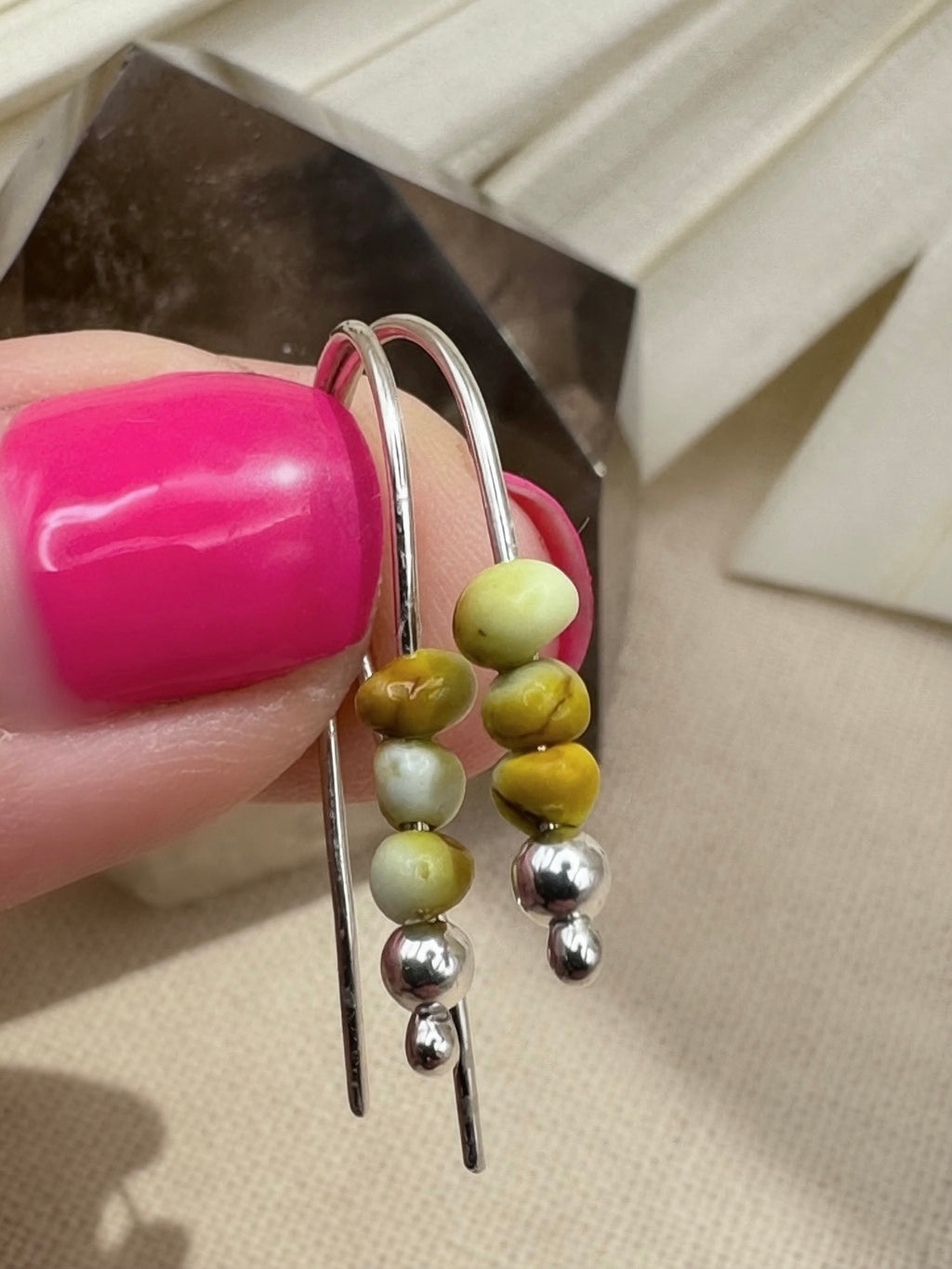 Palomino variscite earrings held by their curved silver wires, showing differing bead colors and earthy markings.