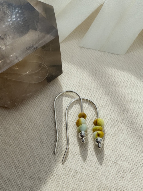 Desert Sprig Palomino variscite earrings on cream fabric, showing yellow-green beads, silver bead accents, and long curved ear wires.