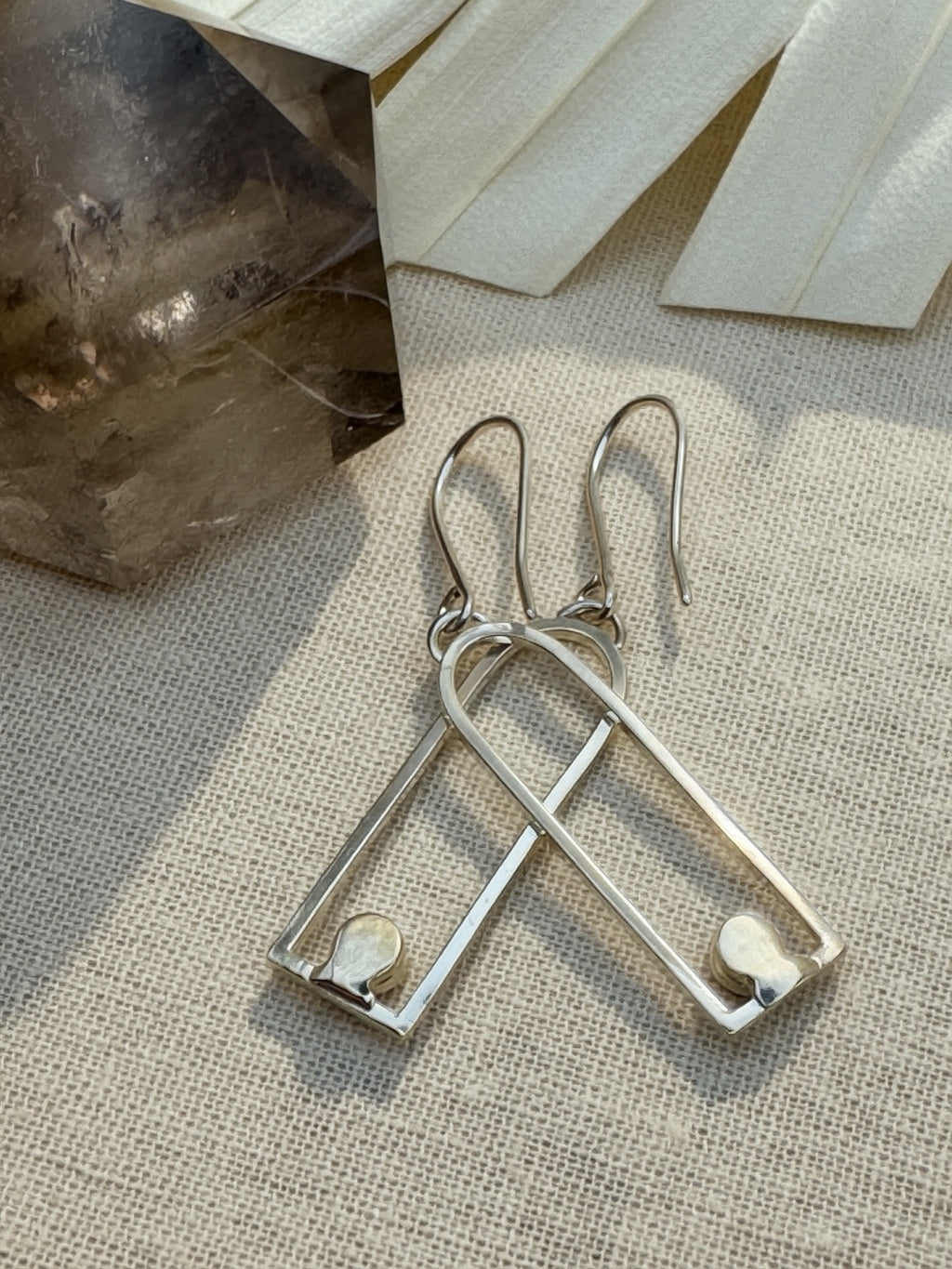Back of the silver arch earrings on cream fabric, showing closed stone settings and open hook ear wires.