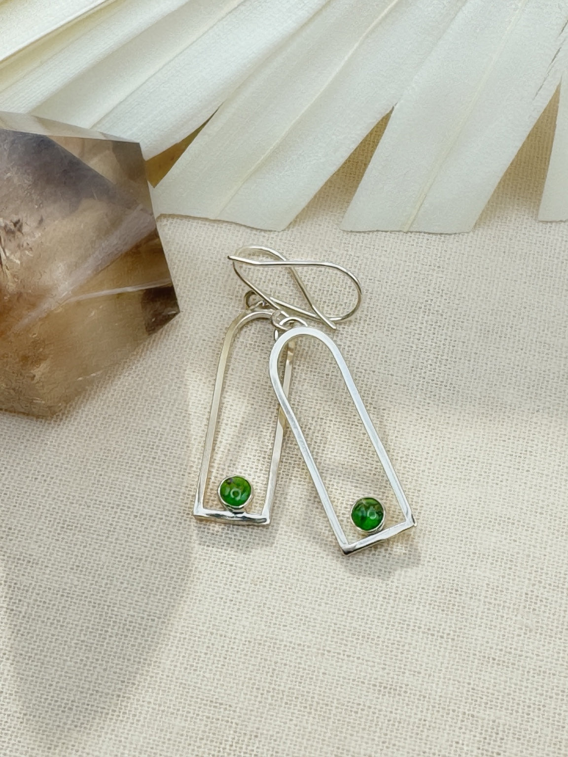 Sonoran Arc earrings on cream fabric, showing elongated open silver arches and round green Sonoran Gold turquoise stones at the base.