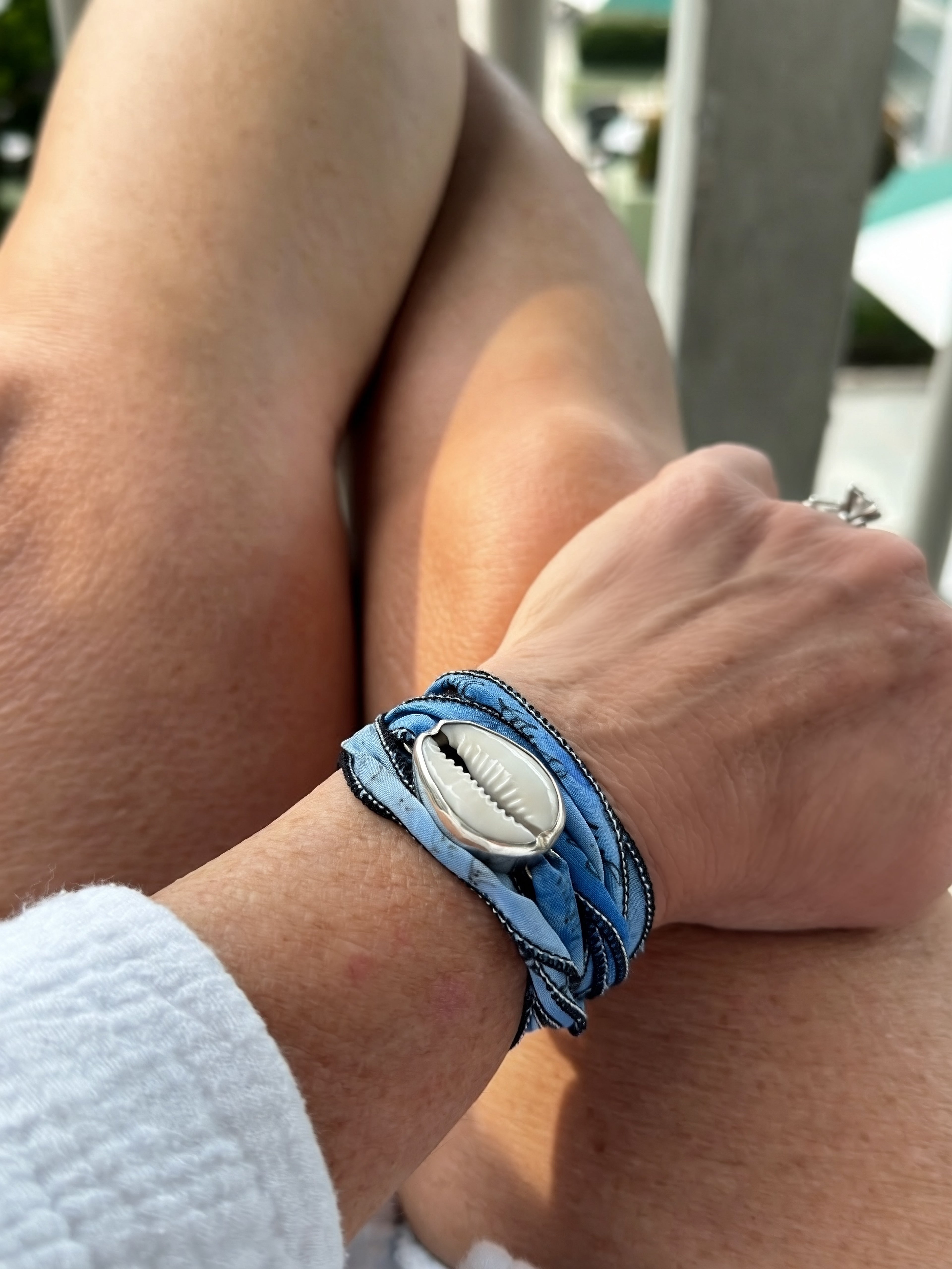 Close-up of a wrist wearing a blue silk bracelet with a cowrie shell in sterling silver 