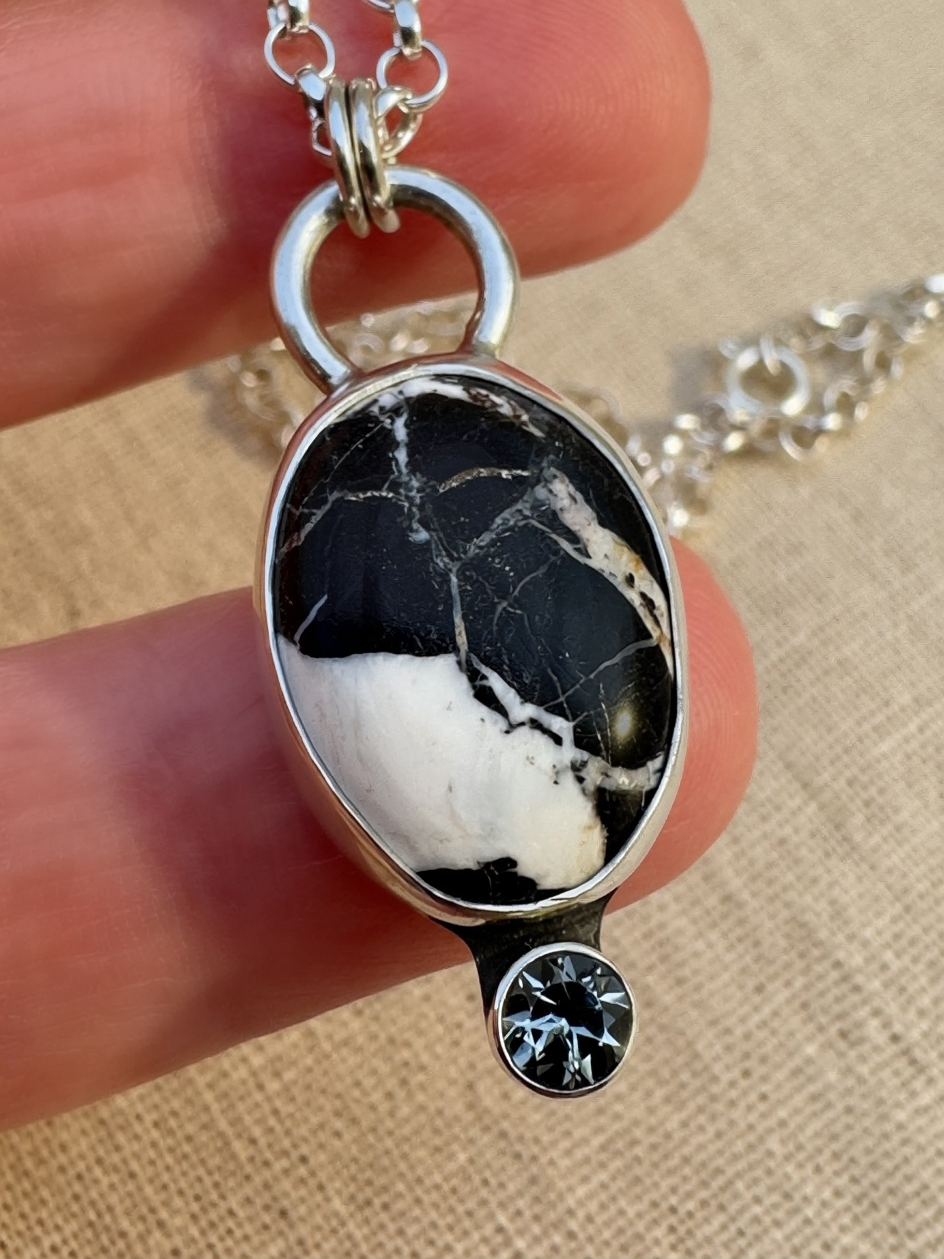 Silver necklace with a white buffalo pendant and gemstone held by a hand on a beige background
