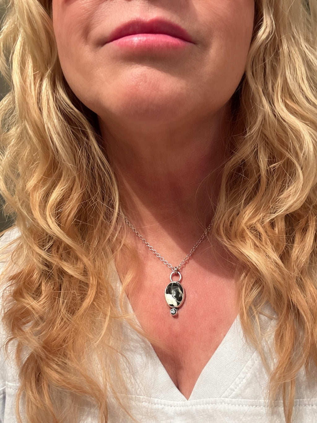 Silver necklace with a white buffalo pendant and gemstone held by a hand on a beige background Being worn