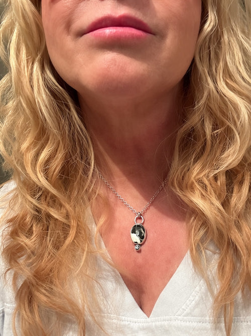 Silver necklace with a white buffalo pendant and gemstone held by a hand on a beige background Being worn