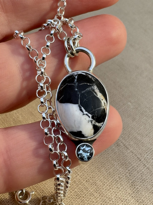 Silver necklace with a white buffalo pendant and gemstone held by a hand on a beige background