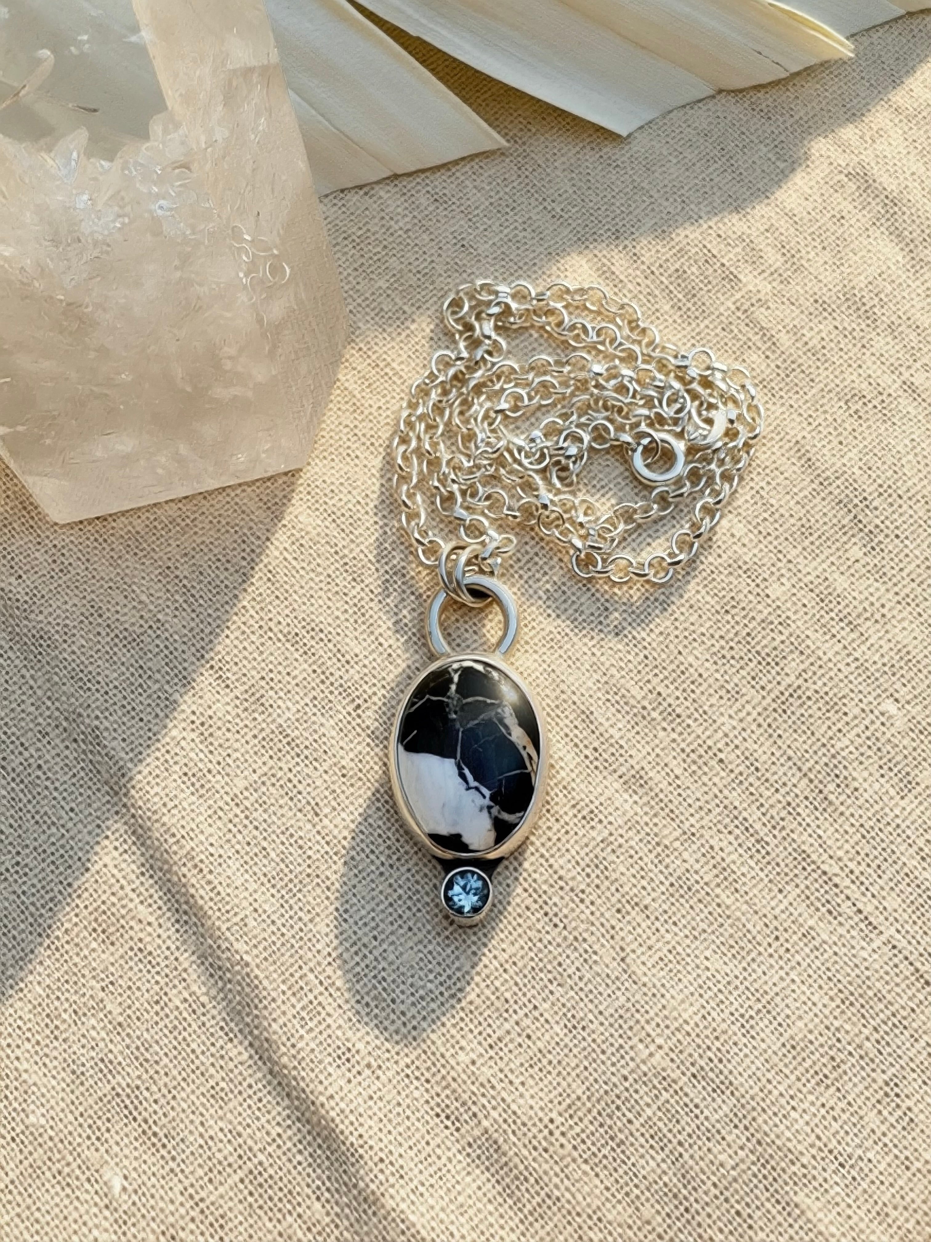 Silver necklace with a white buffalo pendant and gemstone on a beige background