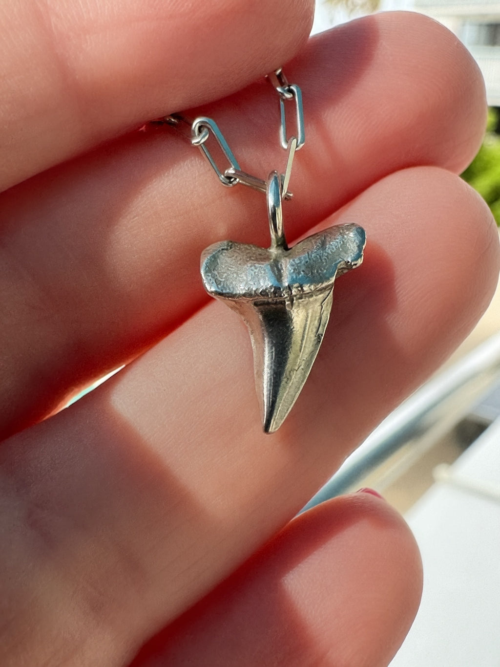 Close-up of cast sterling silver shark tooth pendant showing texture detail, held between fingers with paperclip chain