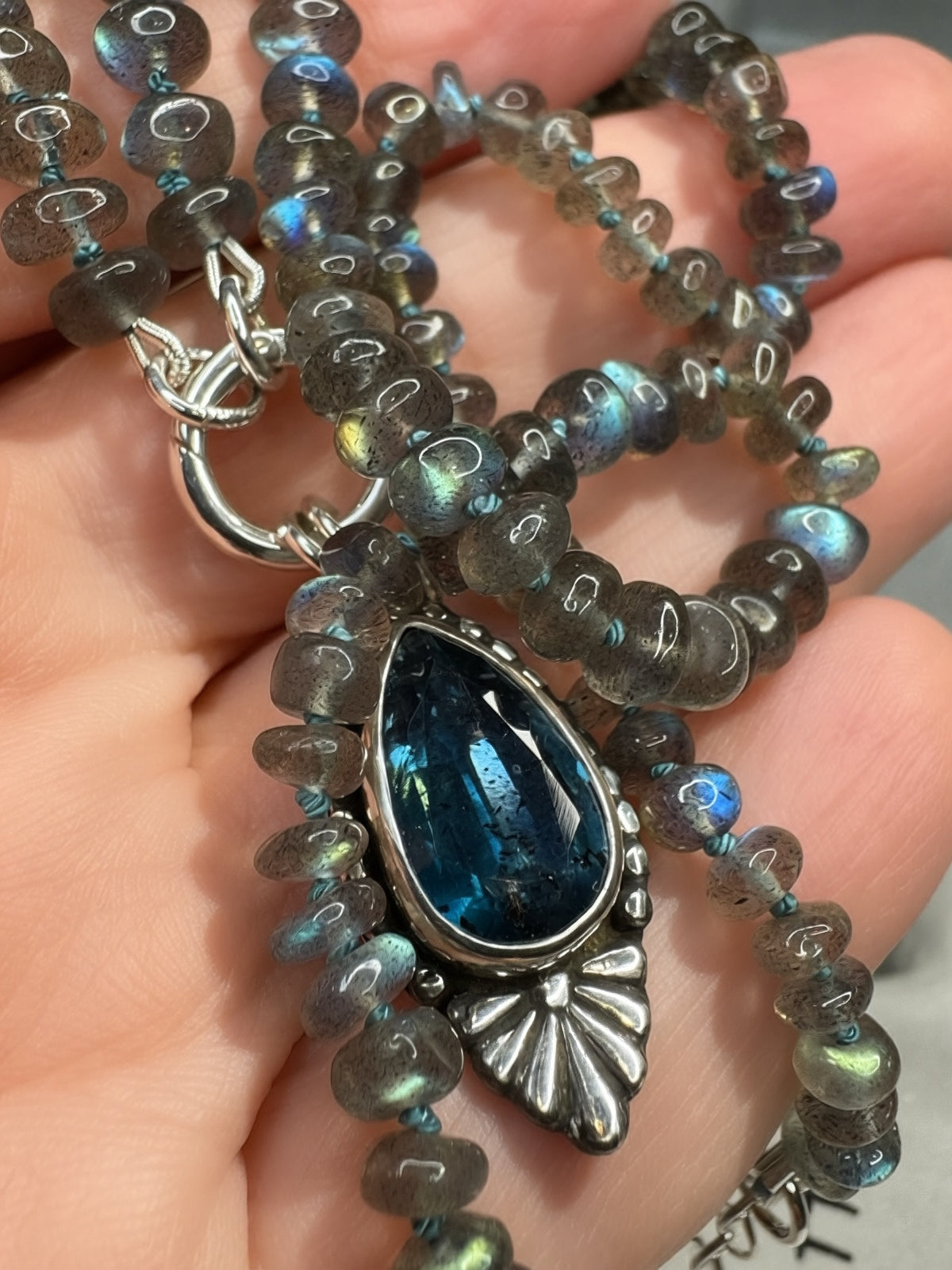 Blue Hour Bloom necklace held in hand, showing the deep teal kyanite, blue-green flashes in the labradorite beads and hand-dyed silk knots.