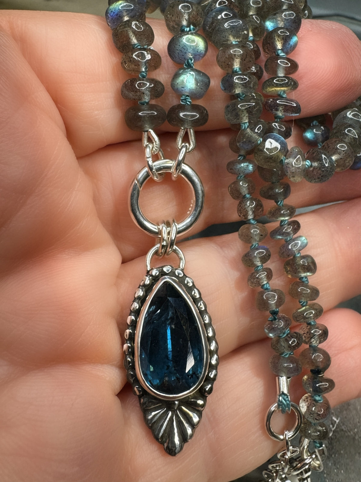 Blue Hour Bloom necklace held in hand, showing the deep teal kyanite, blue-green flashes in the labradorite beads and hand-dyed silk knots.