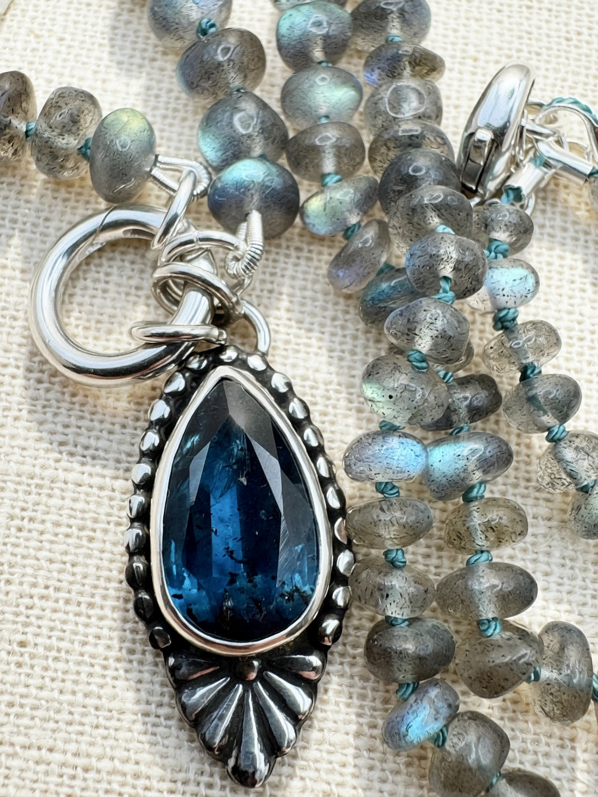 Close-up of the Blue Hour Bloom necklace with a faceted teal kyanite pendant, silver Talavera flower, labradorite beads and charm keeper.