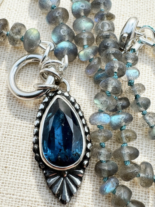 Close-up of the Blue Hour Bloom necklace with a faceted teal kyanite pendant, silver Talavera flower, labradorite beads and charm keeper.