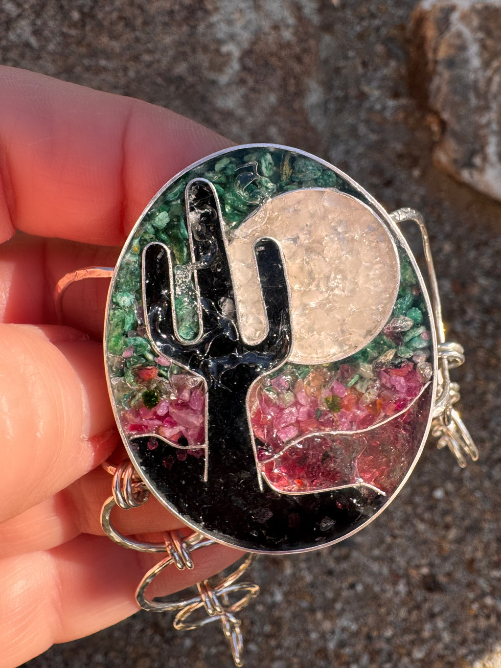 Sterling silver cuff bracelet with cactus and moon design held by a hand against a textured background