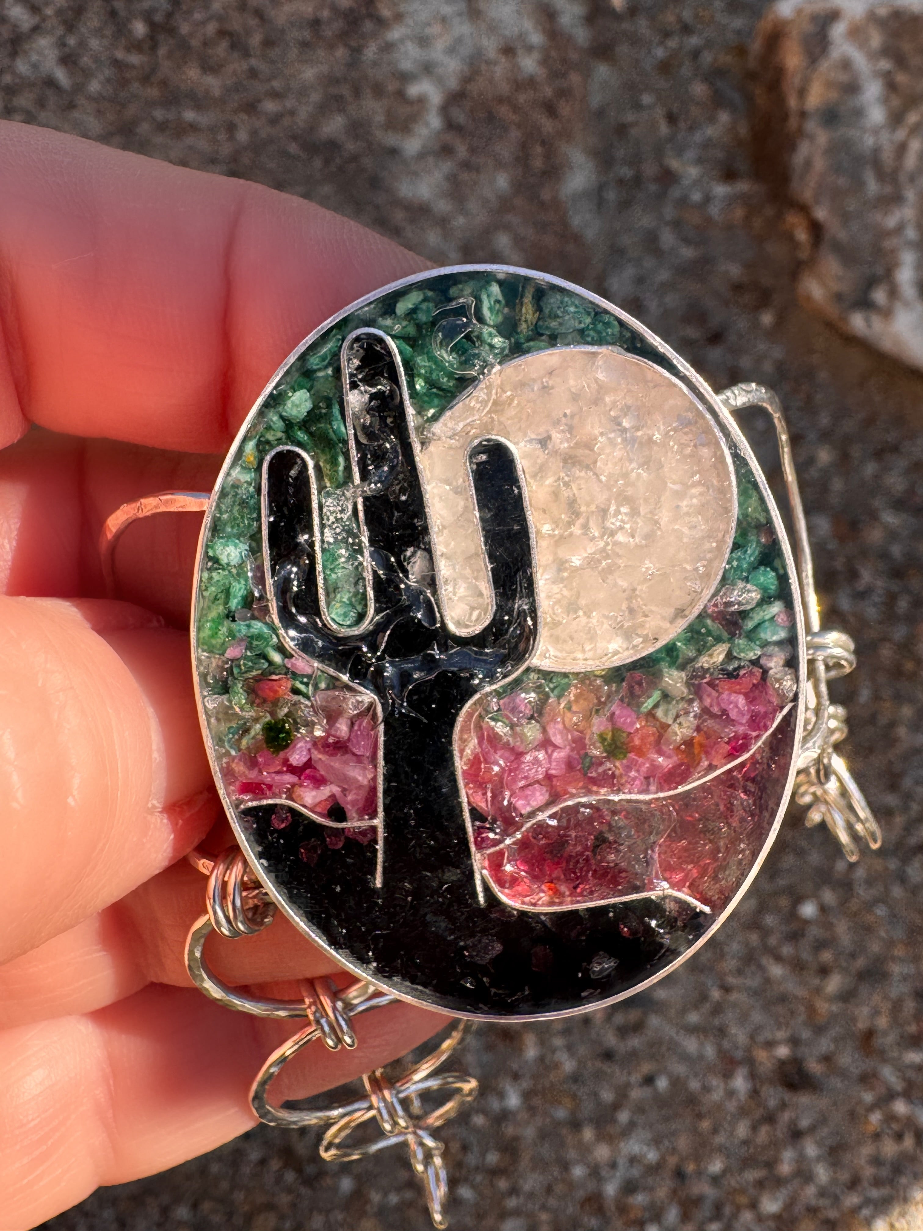 Sterling silver cuff bracelet with cactus and moon design held by a hand against a textured background