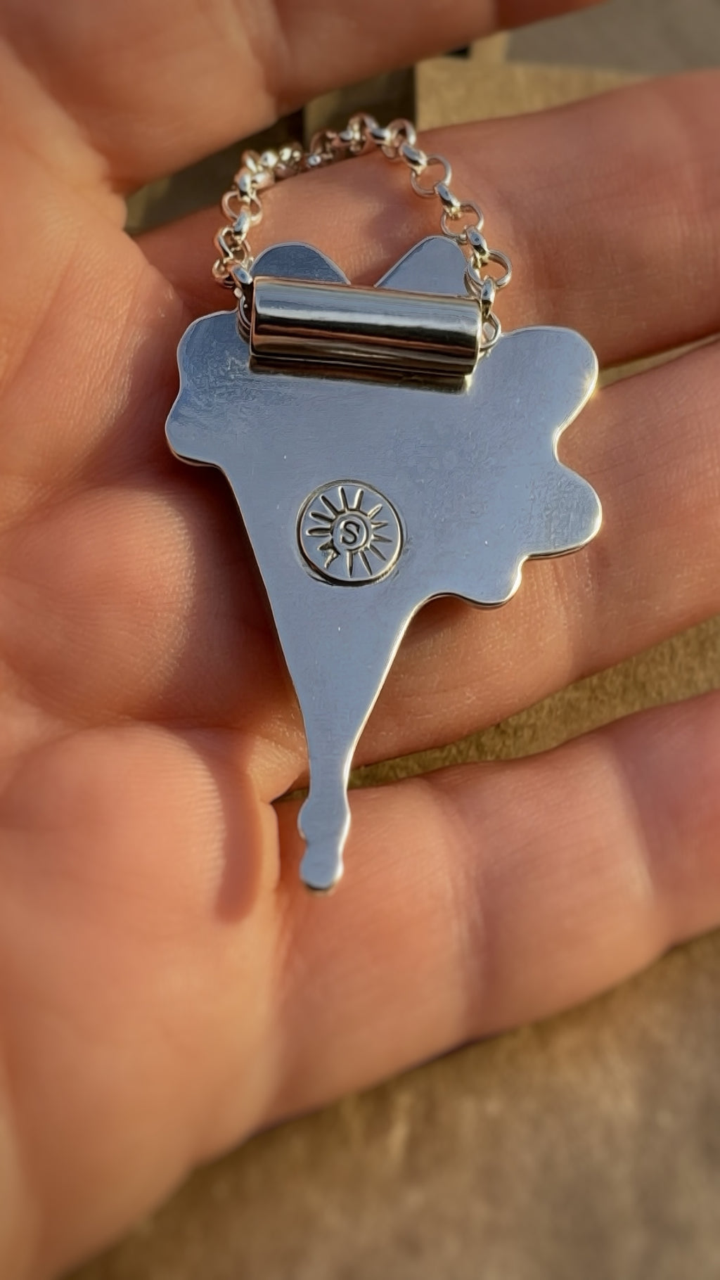 Back view of handmade silver pendant showing maker's mark and polished finish