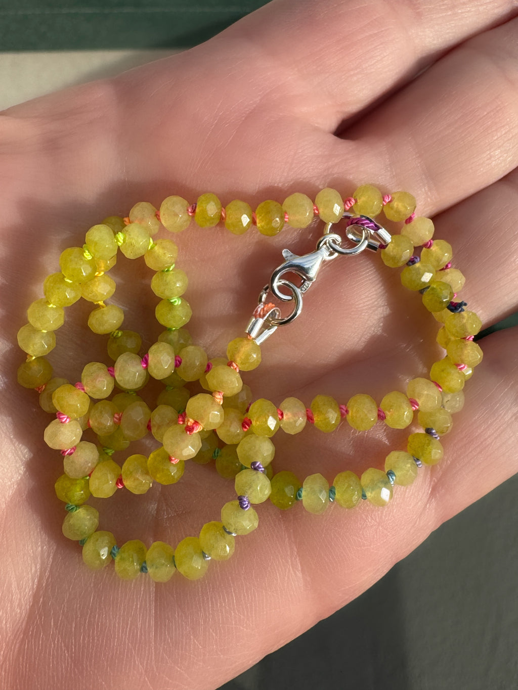 Hand knotted green jade necklace with rainbow silk knots held in palm in natural sunlight showing faceted bead detail
