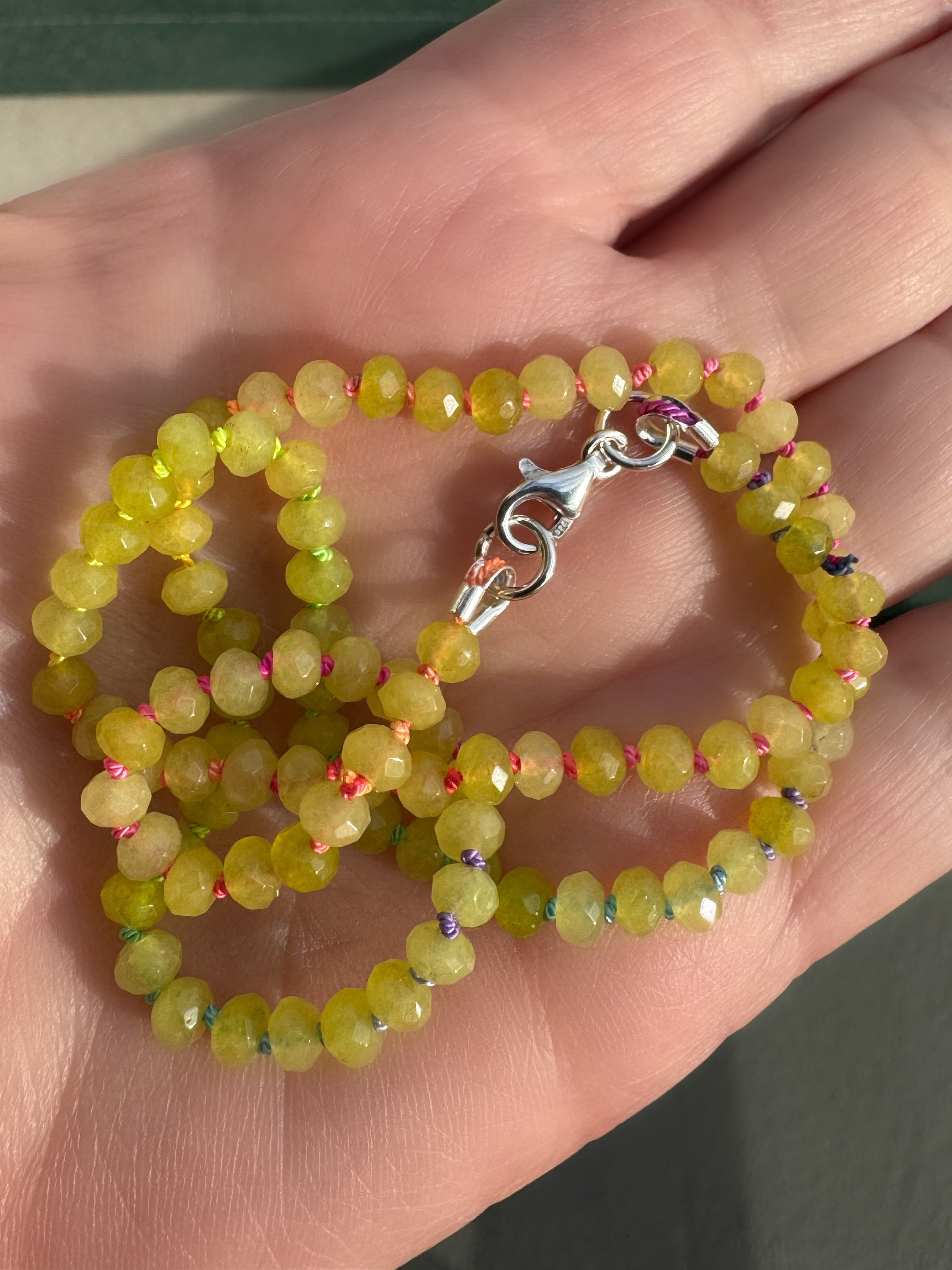 Hand knotted green jade necklace with rainbow silk knots held in palm in natural sunlight showing faceted bead detail