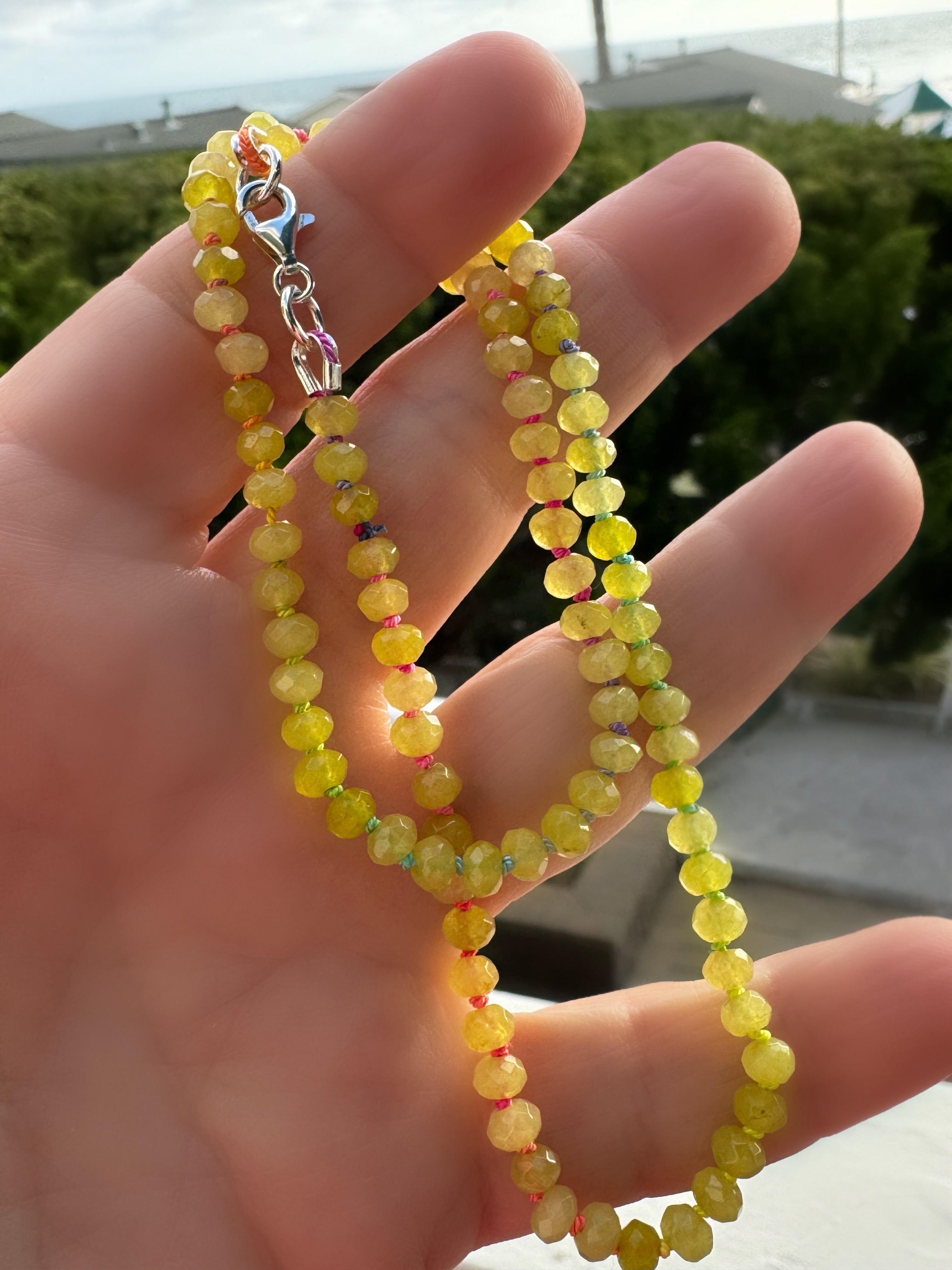 Full length view of faceted candy jade necklace with multicolor silk knots and sterling silver lobster clasp in outdoor light
