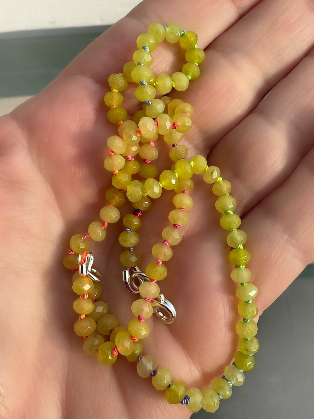 Green beaded necklace held in a hand with a neutral background