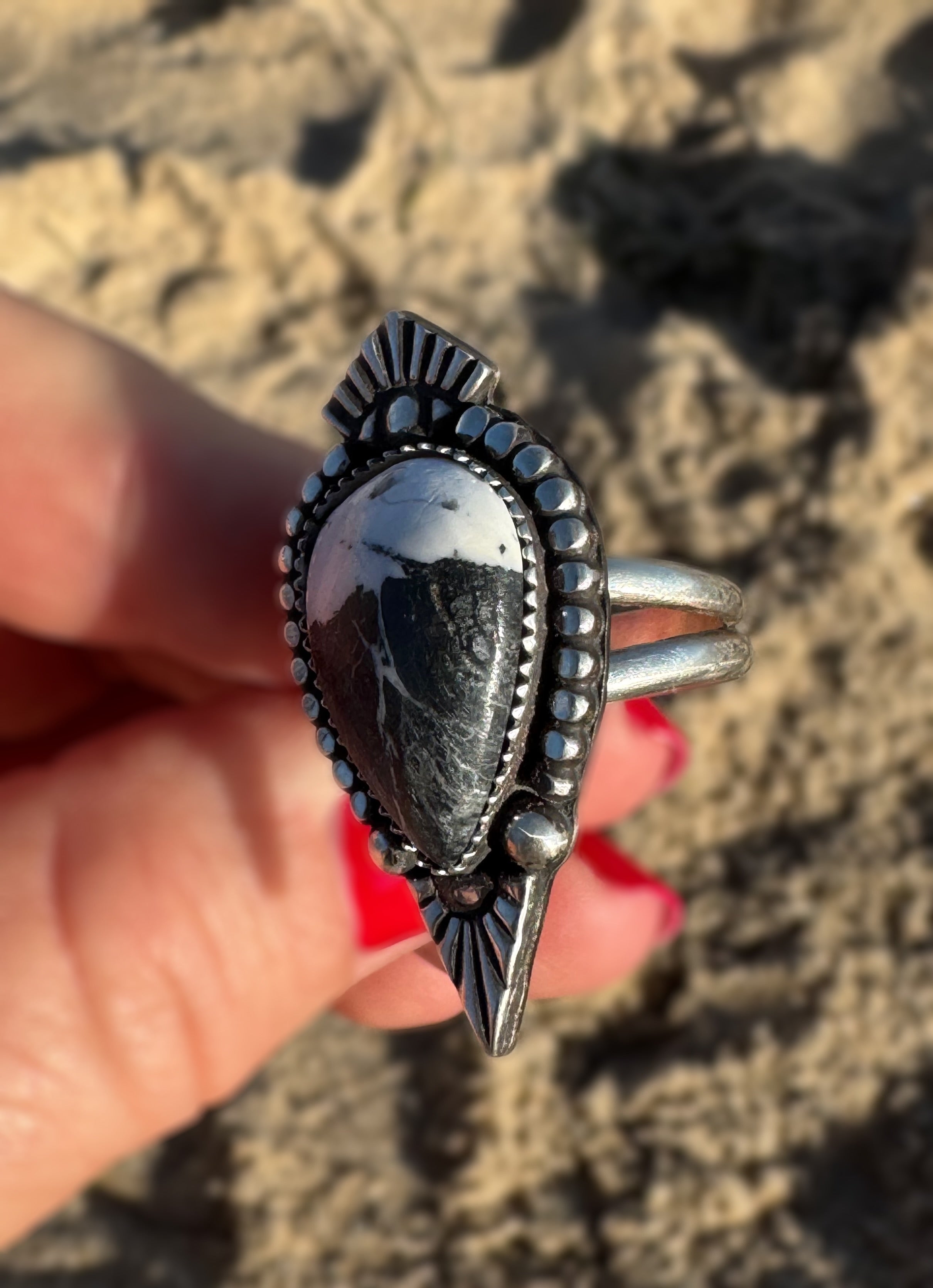 Silver ring with a white buffalo stone held in a hand against a textured beige background