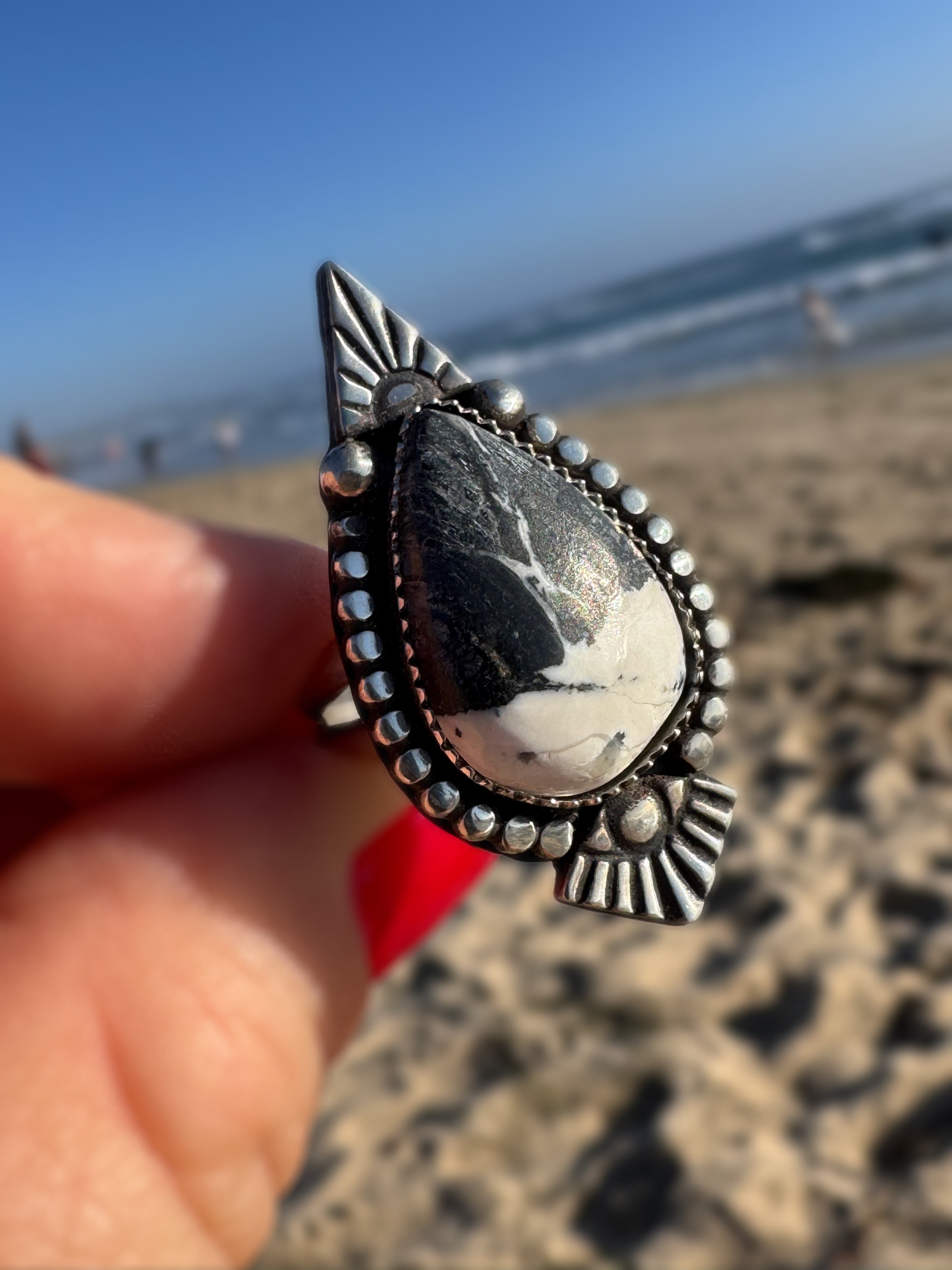 Silver ring with a white buffalo stone held by a hand on a beach.