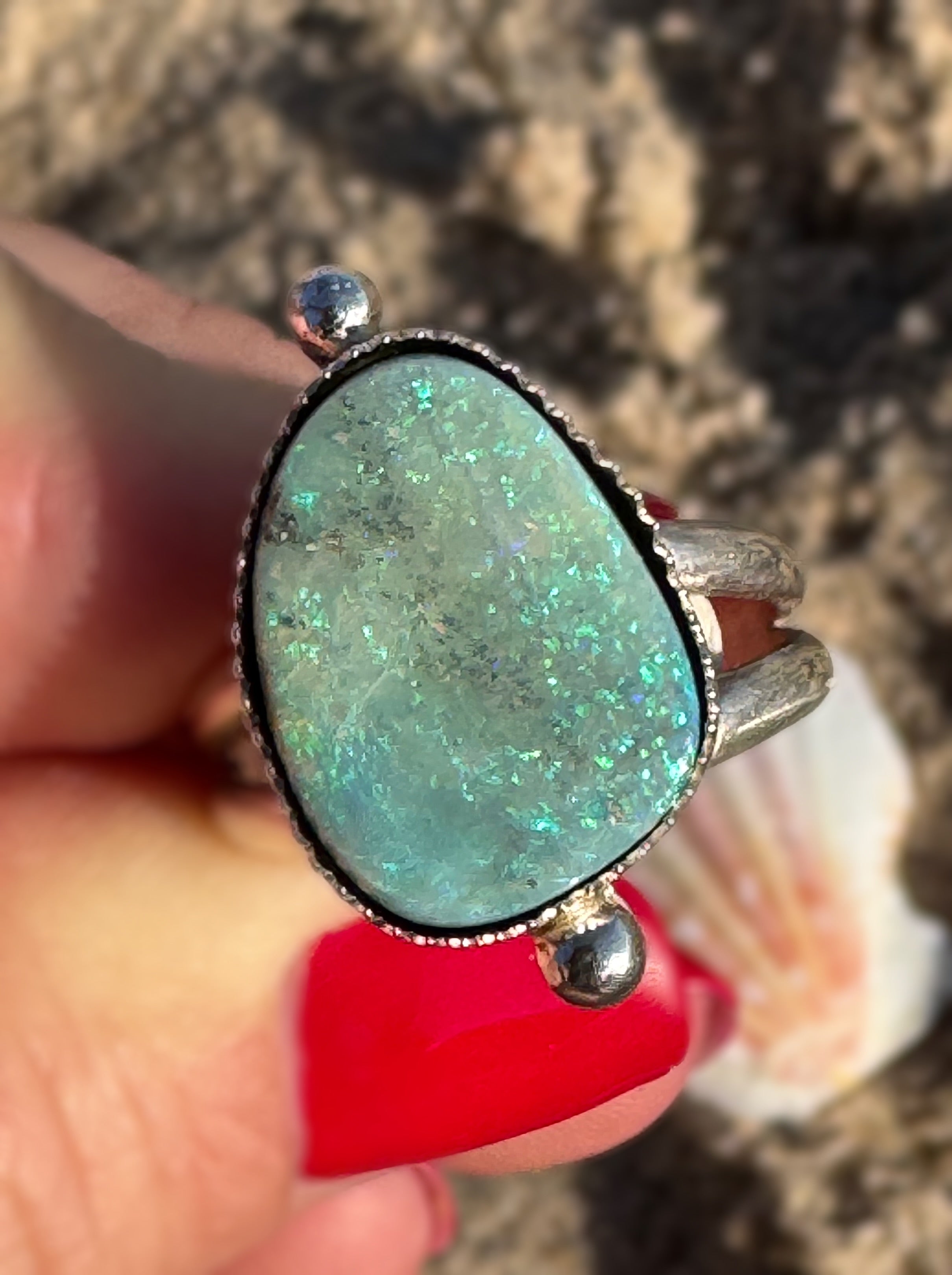 Ring with an opal held in a hand against a blurred natural background